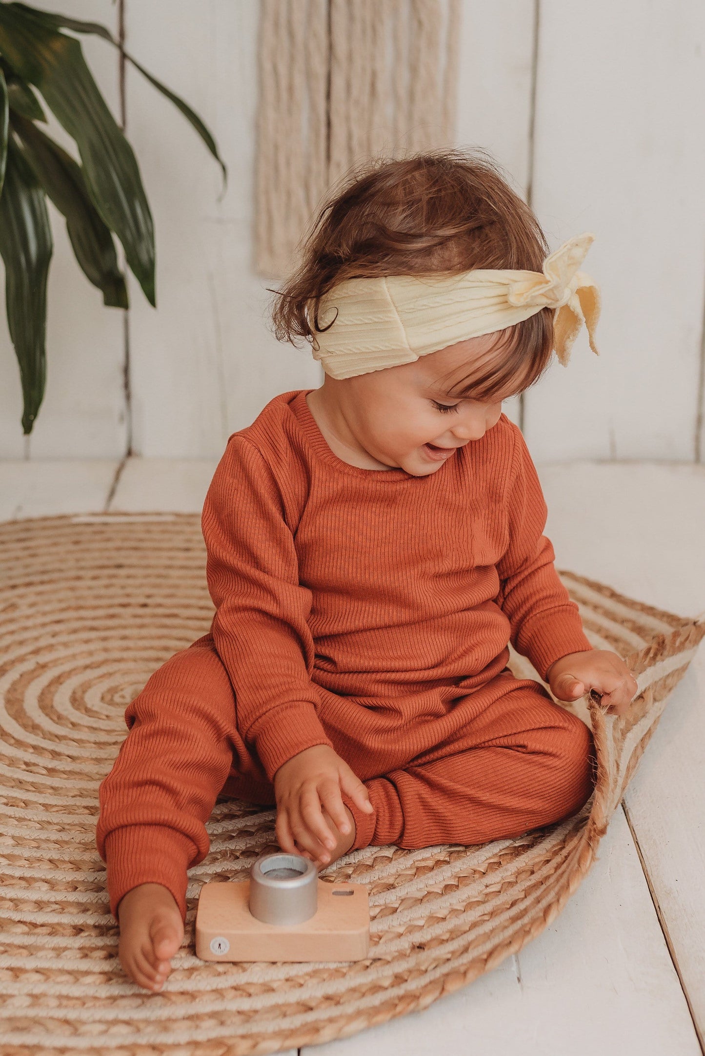 toddler girl sits on boho hippy mat with her handmade lounge comfy set cosy in rust orange leggings lounge jumper sustainable unisex