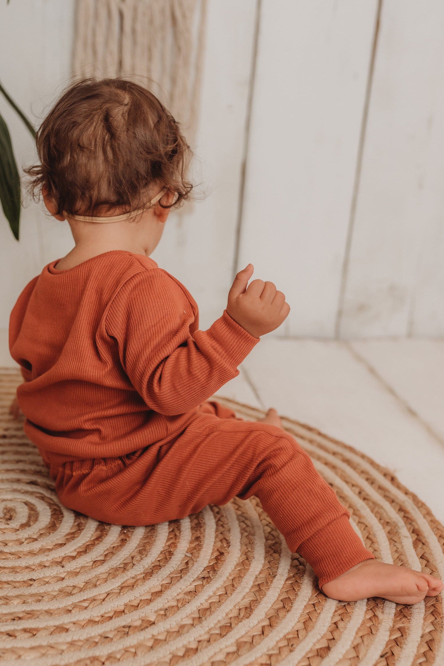 baby girl sits on boho hippy mat with her handmade lounge comfy set cosy in rust orange leggings lounge jumper sustainable unisex