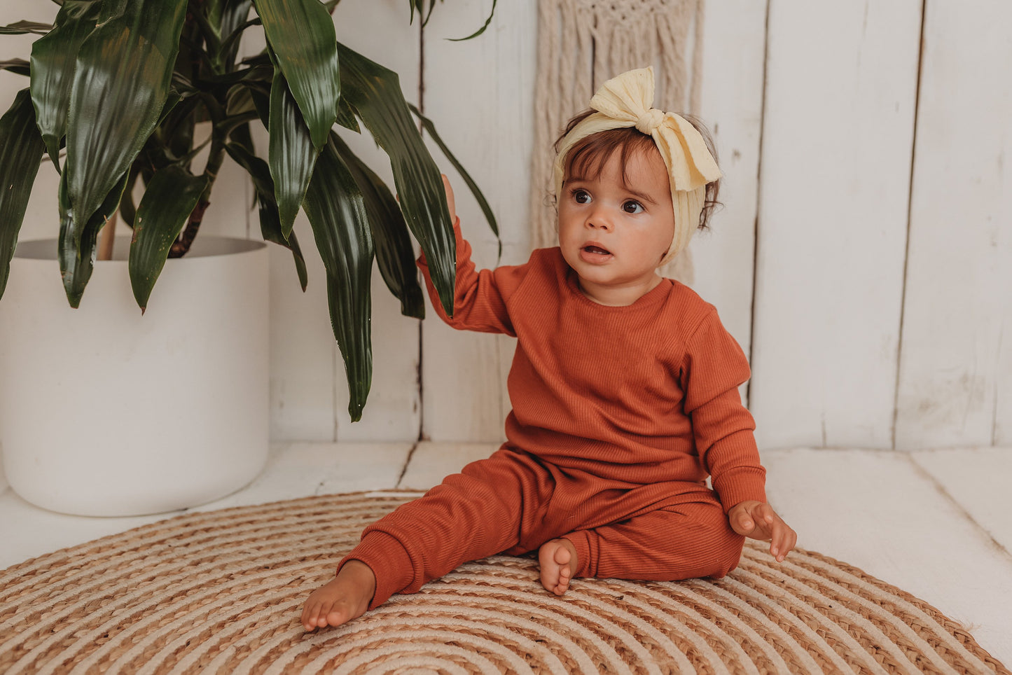 baby girl sits on boho hippy mat with her handmade lounge comfy set cosy in rust orange leggings lounge jumper sustainable unisex