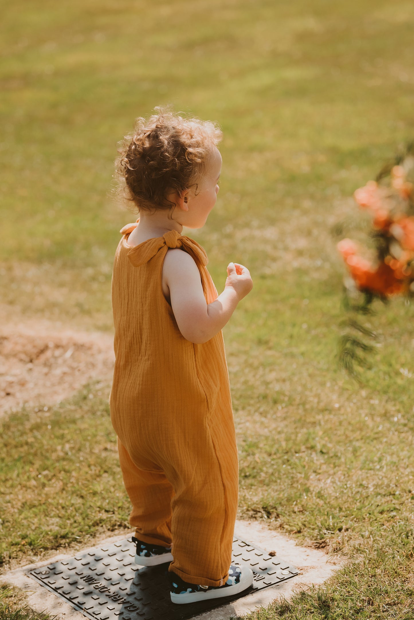toddler boy stands in a field in orange bohemian romper adjustable straps unisex hippy clothing baby girl curly hair sustainable handmade