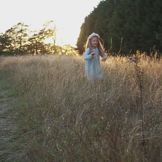 little girl dancing and skipping through meadow with sunset in the background wearing a flower crown wearing her glitter sparkle handmade jersey dress party disco occasion dress inspired frozen elsa sustainable