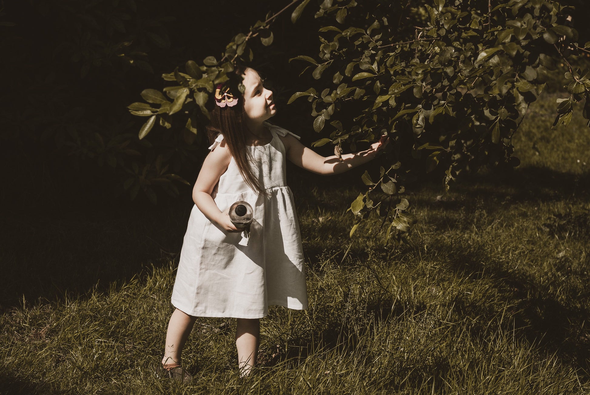 girl stood in garden in summer wearing a cotton linen dress in white adjustable straps sustainable bohemian hippy beach clothing