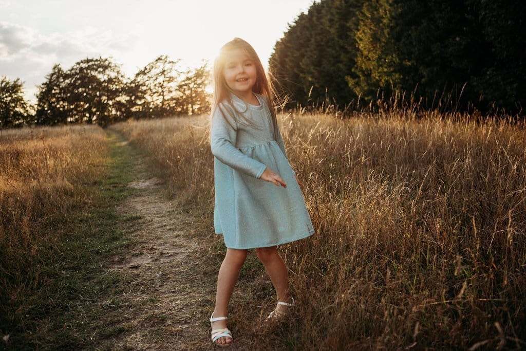 little girl dancing and skipping through meadow with sunset in the background wearing a flower crown wearing her glitter sparkle handmade jersey dress party disco occasion dress inspired frozen elsa sustainable