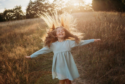 girl flicking her hair back whilst wearing a glitter sparkle party occasion dress in a meadow with the sunset in the background dress inspired by frozen elsa handmade sustainable ethically clothing