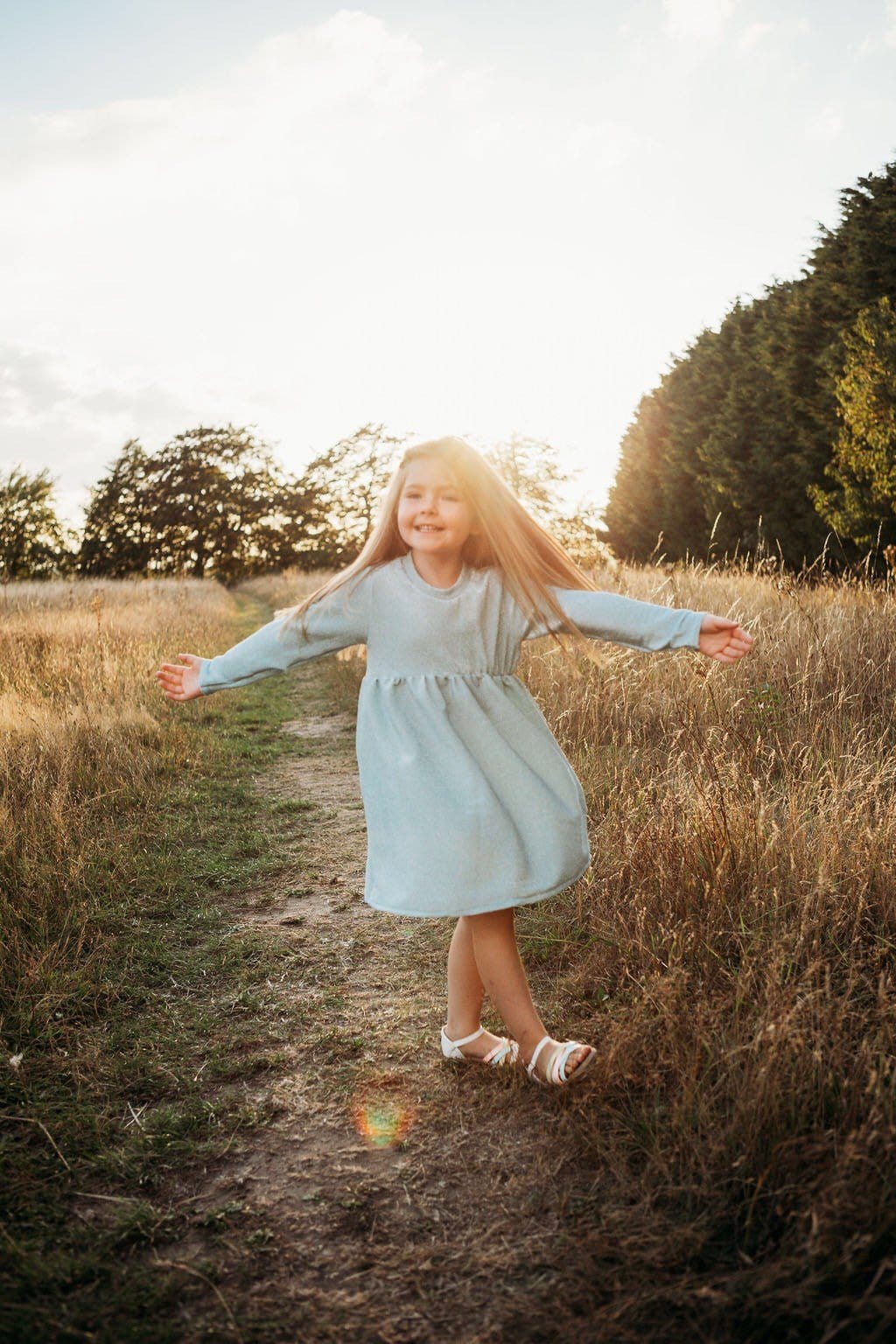 little girl dancing and skipping through meadow with sunset in the background wearing a flower crown wearing her glitter sparkle handmade jersey dress party disco occasion dress inspired frozen elsa sustainable
