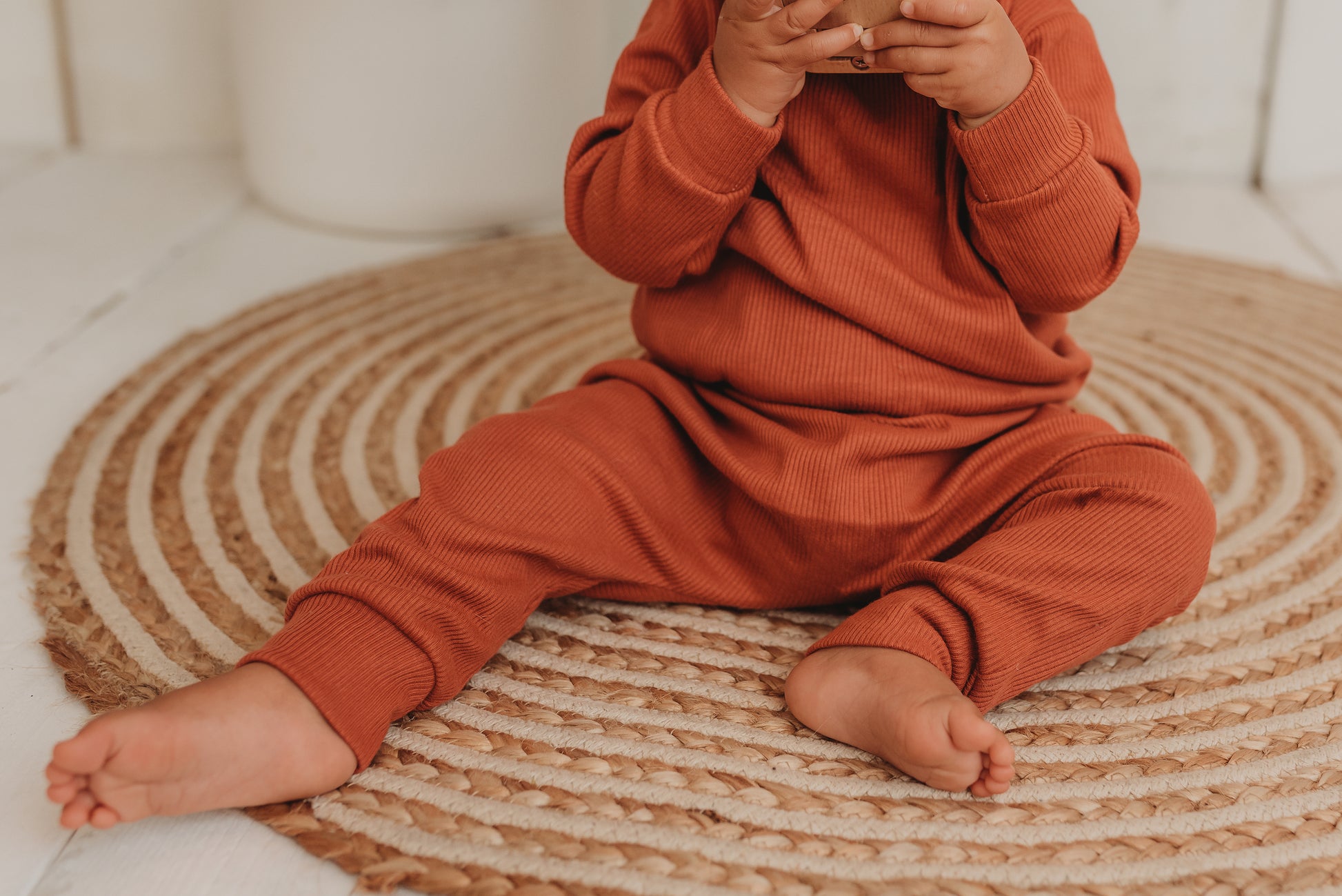 detailed shot of baby girl toddler wearing handamde lounge set in orange rust comfy cosy winter clothing sustainable unisex ribbed fabric