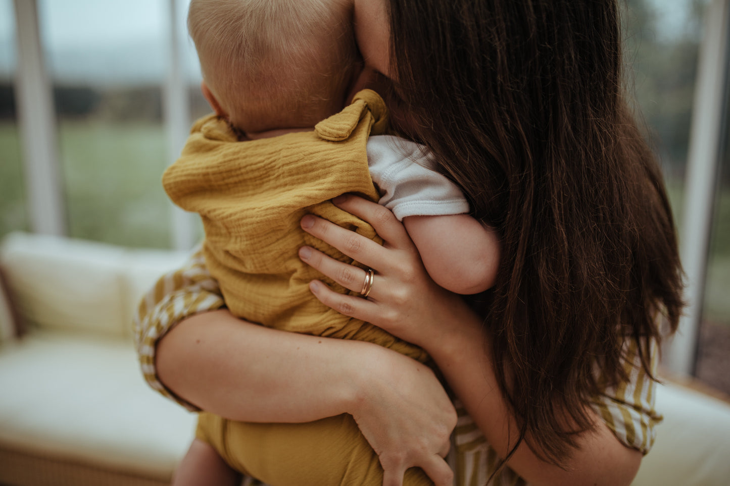 baby boy cuddling mother close up of the harem bohemian romper in ochre with adjustable straps unisex clothing sustainable double gauze muslin