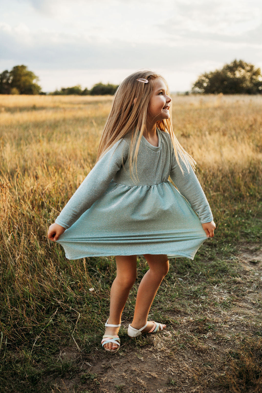 little girl dancing and skipping through meadow with sunset in the background wearing a flower crown wearing her glitter sparkle handmade jersey dress party disco occasion dress inspired frozen elsa sustainable