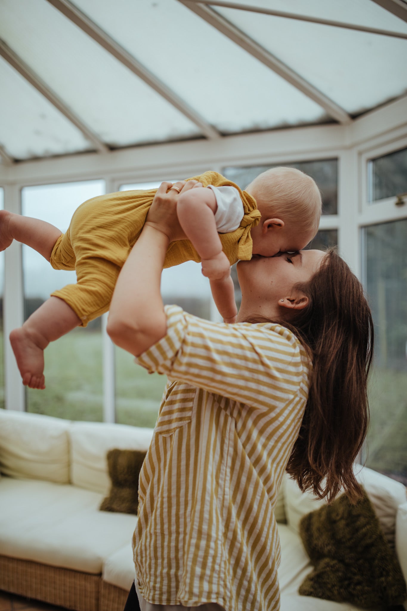 baby boy cuddling mother close up of the harem bohemian romper in ochre with adjustable straps unisex clothing sustainable double gauze muslin