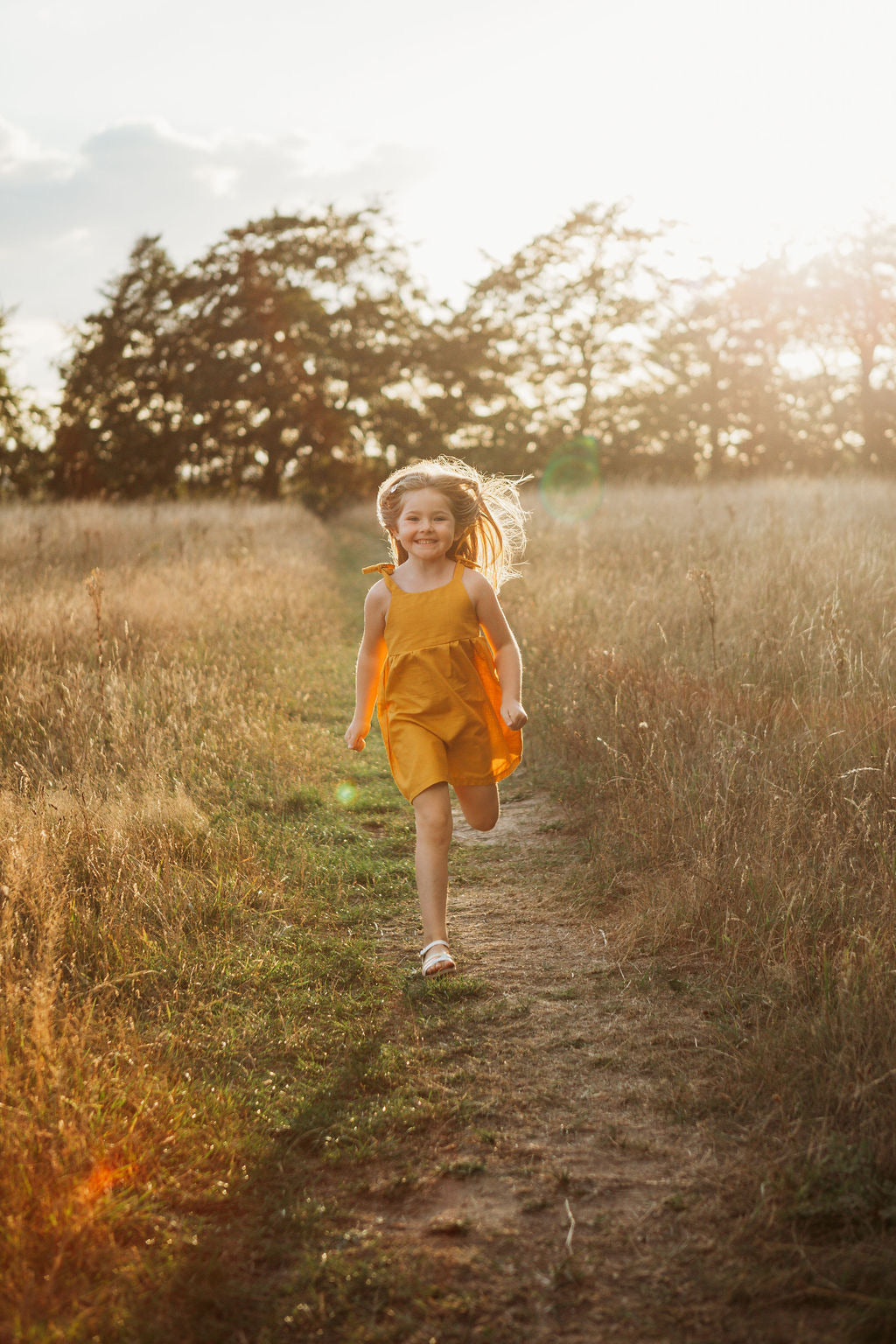 girl dancing in her cotton linen dress in mustard in a field with the sun behind handmade adjustable straps sustainable