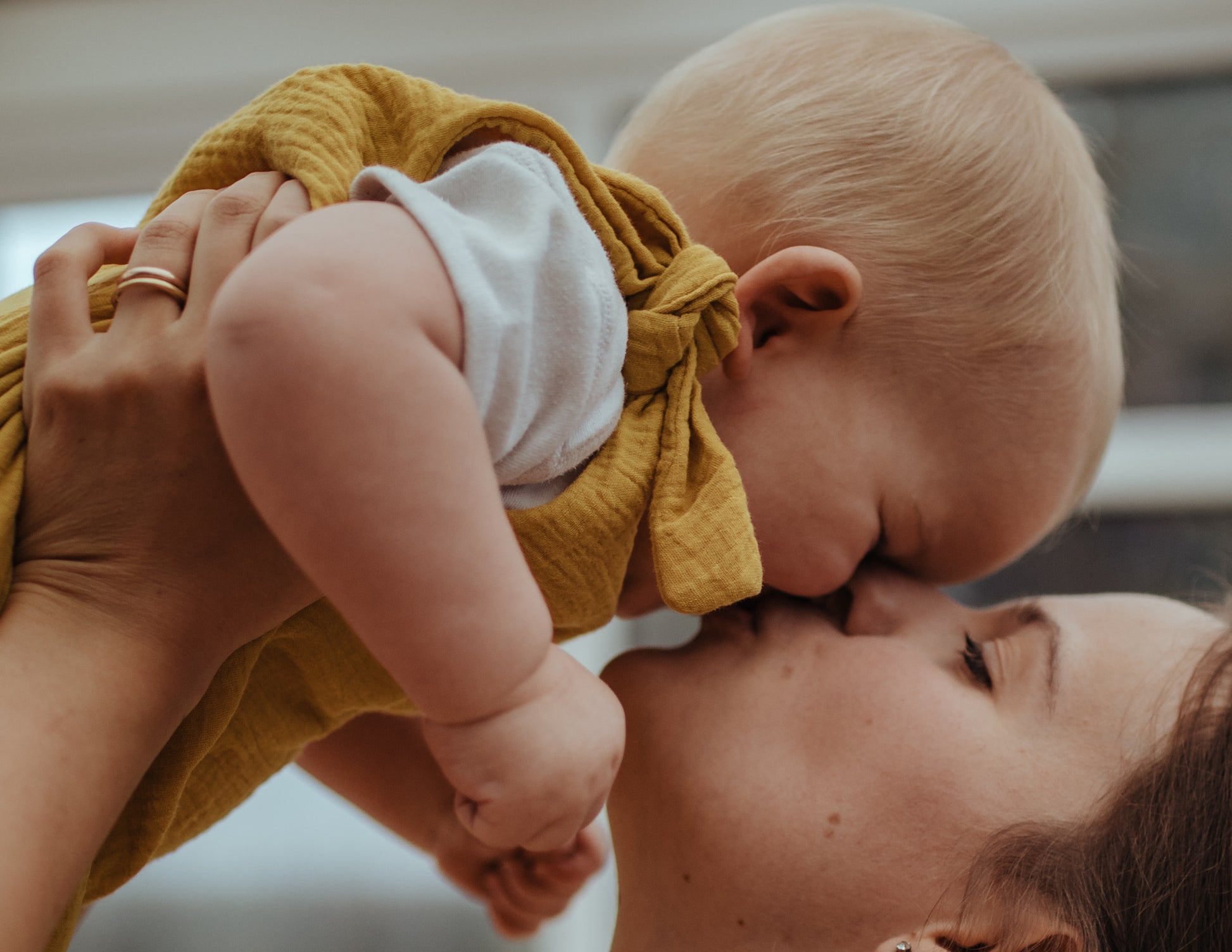 baby boy cuddling mother close up of the harem bohemian romper in ochre with adjustable straps unisex clothing sustainable double gauze muslin